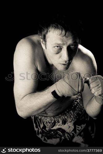 Boxer with a black eye in a battle position. Clenched fists. Dark background.