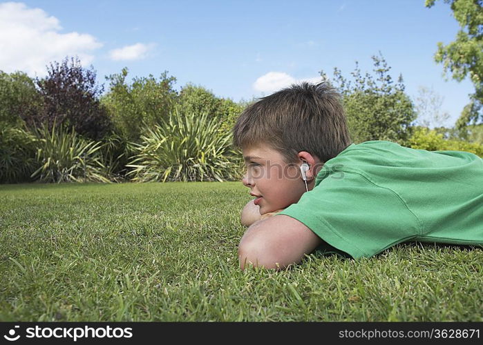 Boy (10-12) lying on elbows in grass, listening to mp3 player