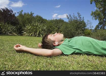 Boy (10-12) lying on grass, listening to mp3 player