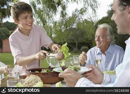 Boy (10-12) serving father at table in garden