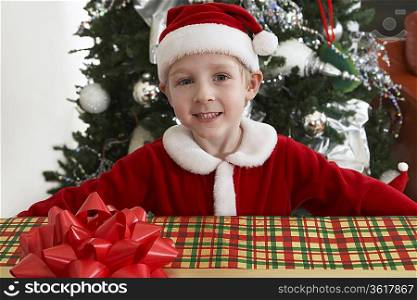 Boy (5-6) in Santa costume holding present by Christmas tree