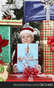 Boy (5-6) in Santa costume in pile of presents by Christmas tree