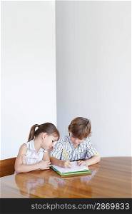 Boy (7-9) and girl (5-6) doing homework together