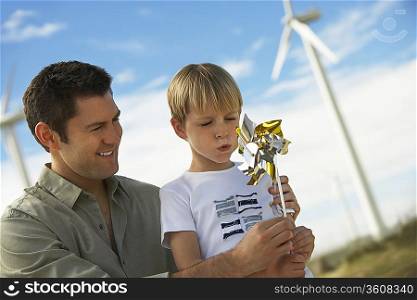 Boy (7-9) blowing toy windmill with father at wind farm