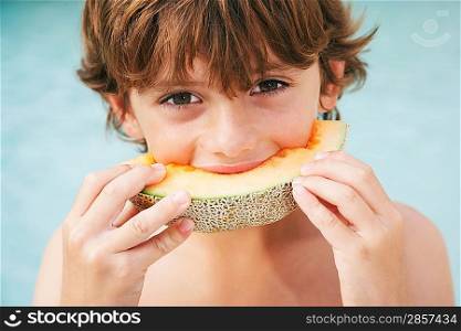Boy (7-9) eating slice of melon close-up