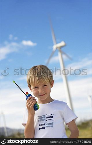 Boy (7-9) holding toy walky-talky at wind farm, portrait