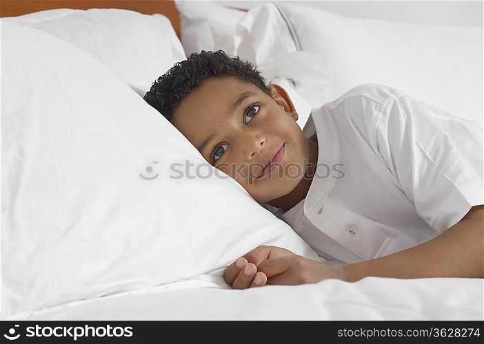Boy (7-9) lying in bed smiling, portrait
