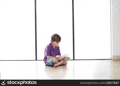 Boy (7-9) sitting on floor playing handheld game