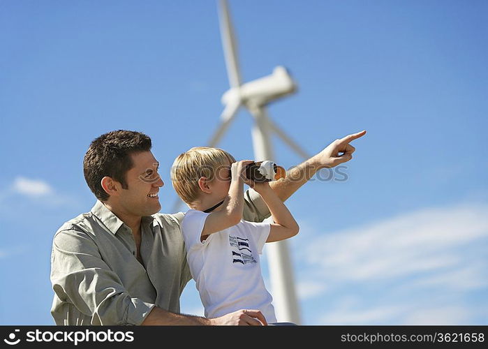 Boy (7-9) using binoculars with father at wind farm