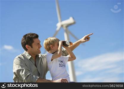 Boy (7-9) using binoculars with father at wind farm