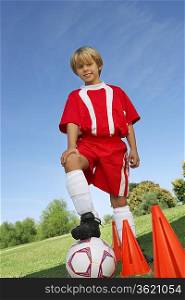 Boy (7-9 years) soccer player holding foot on ball, portrait