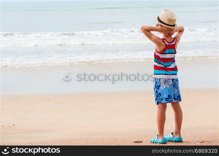 Boy 7 years in a T-shirt and shorts looks at the sea on the beach