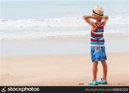 Boy 7 years in a T-shirt and shorts looks at the sea on the beach
