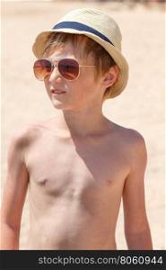 Boy 9 years old in a hat and sunglasses posing on the beach