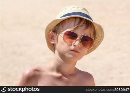 Boy 9 years old in a hat and sunglasses posing on the beach