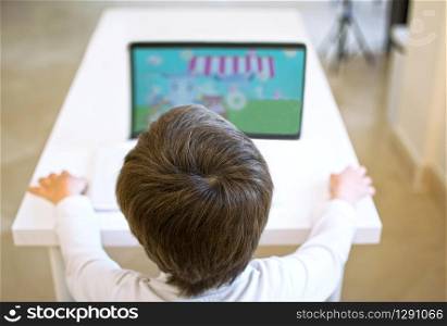 boy alone watching an educative video at the table using his computer and watching videos or playing video games at school.. boy alone watching an educative video at the table using his computer and watching videos or playing video games at school