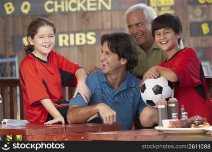 Boy and a girl with their father and grandfather sitting in a restaurant and smiling