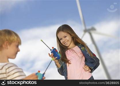 Boy and girl (5-9) playing with walky-talkies at wind farm