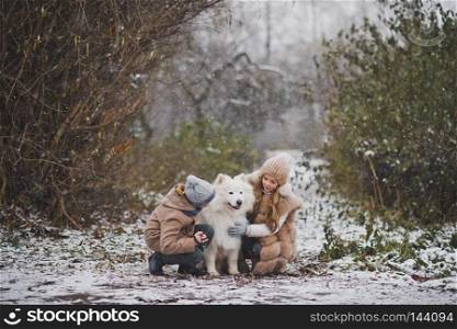 Boy and girl gently petting your beloved Samoyed.. Children on a snowy path playing with the white dog 9842.