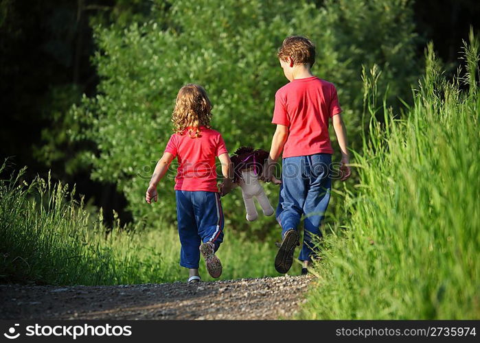 boy and girl go for a walk with doll in park, rear view