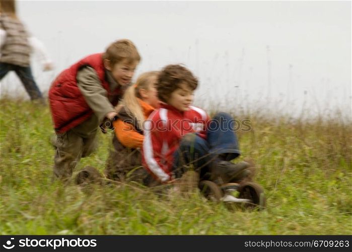 Boy and girl riding a mountain board with a boy pushing them from behind