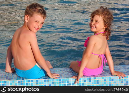 boy and girl sit on border of pool