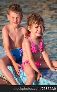 boy and girl sit on border of pool