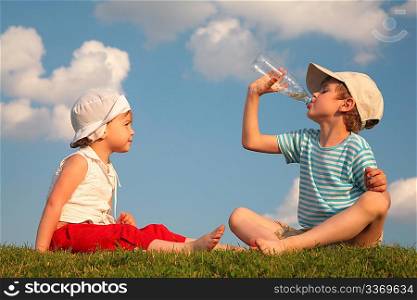 Boy and girl sit on grass and drink from bottle
