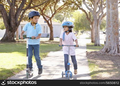 Boy And Girl Wearing Safety Helmets And Riding Scooters
