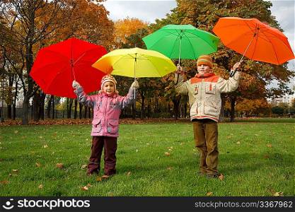Boy and little girl in autumn park. Hold over heads colour umbrellas.