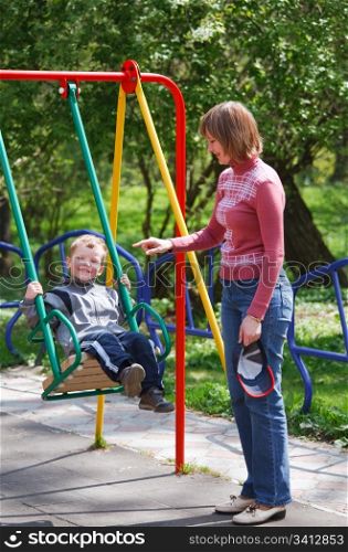 Boy and mother play with swing on may city park (pleasure-ground).