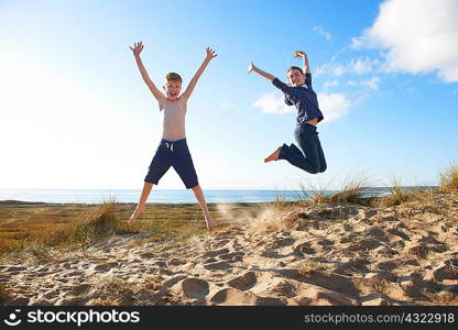 Boy and teenage girl jumping on beach