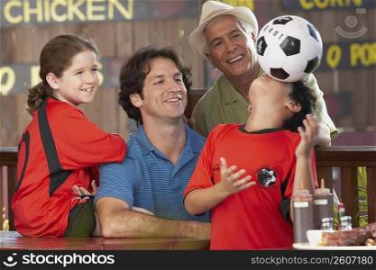 boy balancing a soccer all on his face with his family looking at him