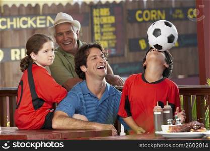 boy balancing a soccer all on his face with his father and sister looking at him