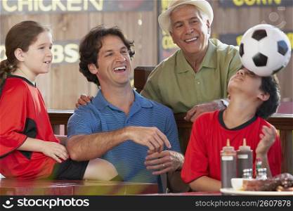 boy balancing a soccer all on his forehead with his family beside him in a restaurant