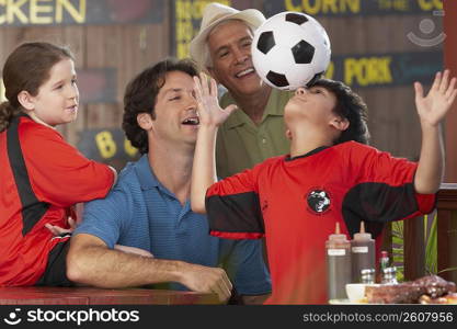 boy balancing a soccer all on his forehead with his family looking at him