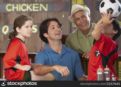 boy balancing a soccer all on his head with his family looking at him