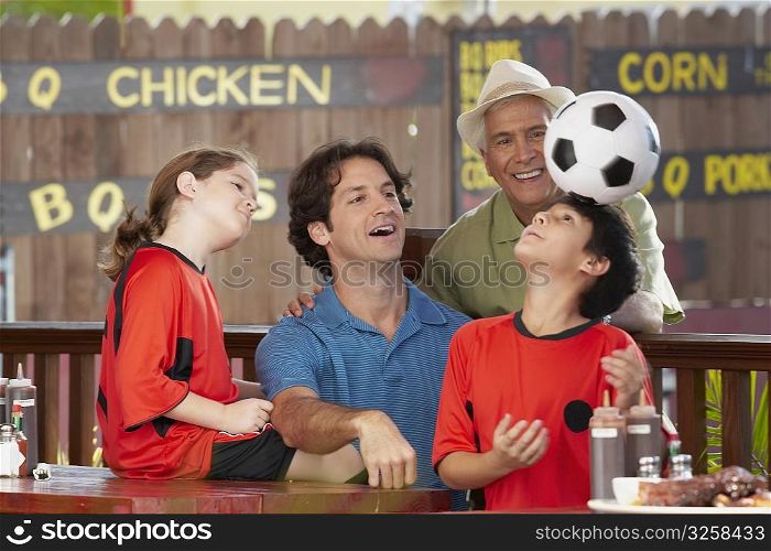boy balancing a soccer all on his head with his family looking at him
