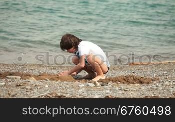 Boy builds a free form sandcastle on the summer beach