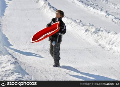 boy carrying his sled down the hill with snow background