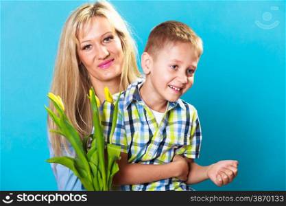 Boy celebrating mother&#39;s day. little child lad giving flowers yellow tulips to his mom mother studio shot on blue