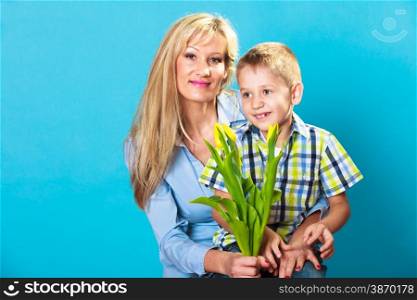 Boy celebrating mother&#39;s day. little child lad giving flowers yellow tulips to his mom mother studio shot on blue