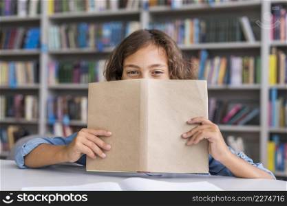 boy covering his face with book library
