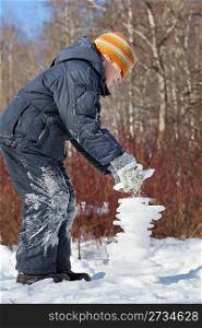 boy creates pyramid from ice in sunny day in winter in wood, Unstable balance