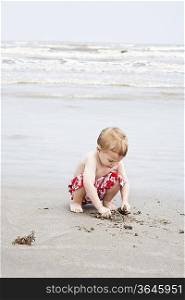 Boy crouching and playing with sand at water&acute;s edge