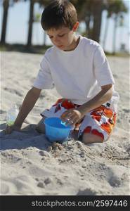Boy crouching and playing with sand on the beach