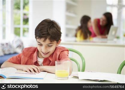 Boy Doing Homework As Mother And Daughter uses Laptop