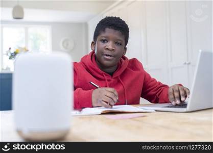 Boy Doing Homework At Home Asking Digital Assistant Question