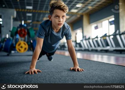 Boy doing push up exercise in gym, front view. Youngster on training in sport club, healthcare and healthy lifestyle, schoolboy on workout, sportive youth. Boy doing push up exercise in gym, front view