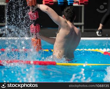 Boy Doing Water Aerobics with Floating Pool Dumbbells Outdoor in a Swimming Pool.. Boy Doing Water Aerobics with Floating Pool Dumbbells Outdoor in a Swimming Pool